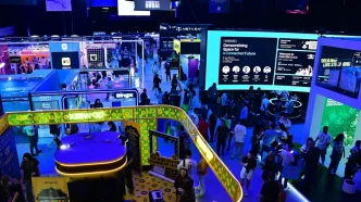 Wide view of a crowded tech expo floor with neon-lit booths, large digital screens, and attendees exploring colorful displays and kiosks.