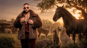 A man in a fur coat and sunglasses stands with a dog, a cat, and a horse in a sunset pasture.