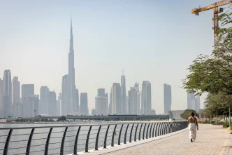 A person walking along a waterfront promenade with the Dubai skyline behind