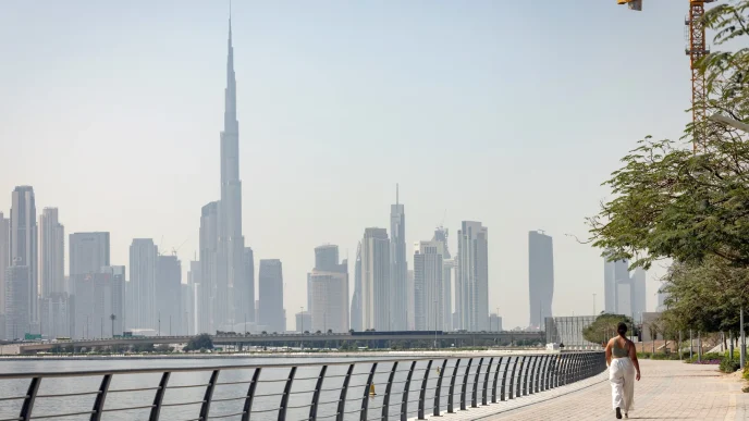 A person walking along a waterfront promenade with the Dubai skyline behind