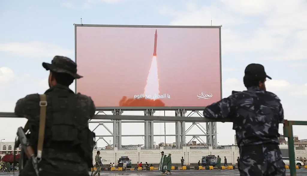 Armed fighters watching a missile launch displayed on a large screen