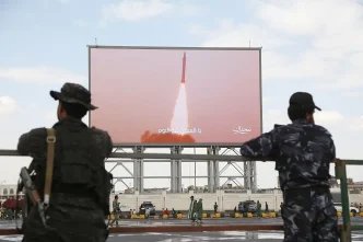 Armed fighters watching a missile launch displayed on a large screen