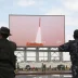 Armed fighters watching a missile launch displayed on a large screen