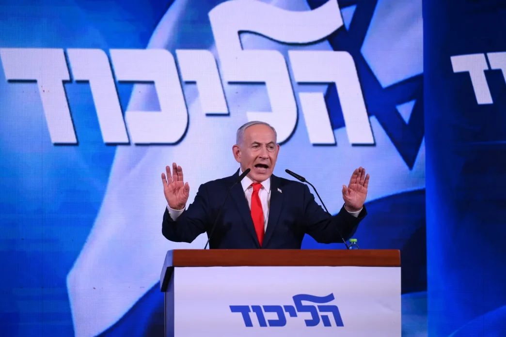 Benjamin Netanyahu speaking at a podium with raised hands at a Likud rally