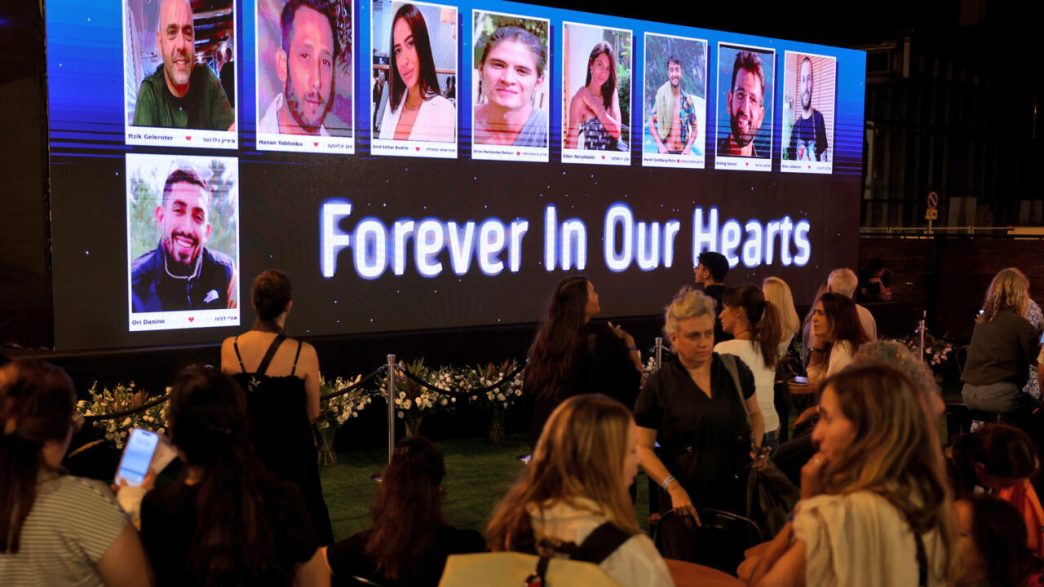 Mourners gather before a memorial screen displaying photos of October 7 victims