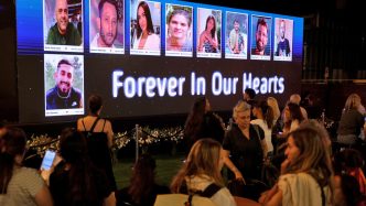 Mourners gather before a memorial screen displaying photos of October 7 victims